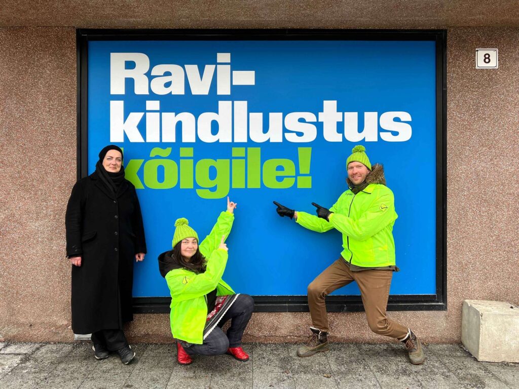 Piret Räni, Hannes Liitmäe ja Elin Kard (EKL) plakati "Ravikindlustus kõigile!" ees
